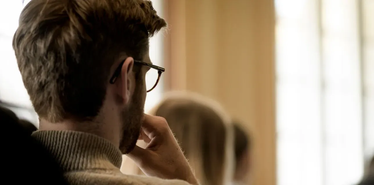 Student i ett klassrum, snett bakifrån. Foto.